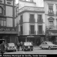 Aspecto de la Campana a principios de los años 60 del siglo XX. Automóviles aparcados en las inmediaciones de los comercios que comparten una misma denominación comercial: la confitería, la óptica y la pañería. ©ICAS-SAHP, Fototeca Municipal de Sevilla, fondo Serrano