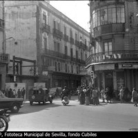 Tráfico intenso en la confluencia de las calles San Eloy, O´Donnell y la Campana. El edificio del Gran Café de París ya sólo conserva la fachada original de los pisos superiores, mientras que el bajo lo ocupa, ya remozado, el Banco Hispano Americano. A la derecha el Bar Flor con anuncios de nostálgicas bebidas como Calisay y Mirinda. 1961 ©ICAS-SAHP, Fototeca Municipal de Sevilla, fondo Cubiles