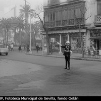 Un guardia urbano infantil dirige una carrera de bicicletas y karts en el centro de la ciudad con motivo de la fiesta de la Policía Municipal. En la esquina con plaza del Duque, el establecimiento de fotografía Pinto, la sombrerería Padilla y el bar Pinto, propiedad de Pepe Pinto y la Niña de los Peines. 1968 ©ICAS-SAHP, Fototeca Municipal de Sevilla, fondo Gelán